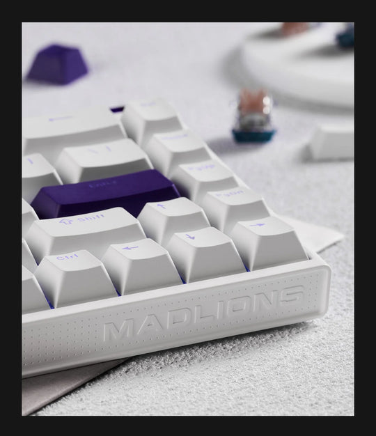 Close-up of a white keyboard with purple keycaps on a light gray surface.